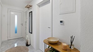 Ein Flur mit einer weißen Tür, einem Spiegel, einem digitalen Thermostat, einem kleinen Tisch mit Schale und Kerze sowie einer Topfpflanze.