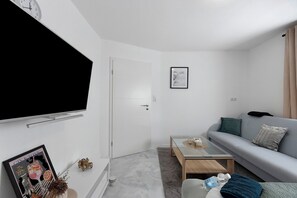 Una sala de estar moderna con un televisor de pantalla plana montado en la pared, un sofá gris, una mesa de centro y un cuadro enmarcado.