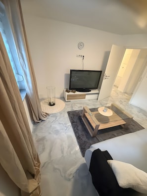 Ein modernes Hotelzimmer mit einem Flachbildfernseher, einem Glastisch, einer Couch und einem Bett.
