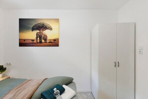 Une chambre à coucher avec un lit, une armoire et un tableau représentant un éléphant et un arbre.