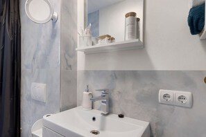 Un baño con lavamanos blanco, espejo y repisas con artículos de aseo.