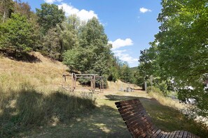 Un parc avec une balançoire en bois, un banc et une zone herbeuse bordée d’arbres.