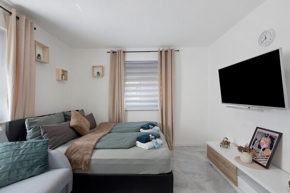 Un dormitorio moderno con cama, televisión y ventana con cortinas.