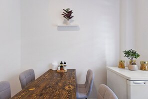Un comedor con mesa de madera, sillas, un armario blanco y objetos decorativos como una planta y frascos.