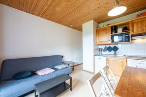 Un espace de vie compact comprenant un canapé, une petite table, une table à manger en bois et un coin cuisine avec des meubles et des appareils électroménagers en bois.
