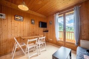 Een houten interieur met een tafel, stoelen, een televisie en een raam met uitzicht.