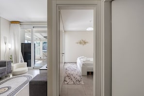 Ein Hotelzimmer mit Bett, einer Sitzecke mit Sofa und Sessel, einem großen Fenster und einem Flur, der in ein weiteres Zimmer führt.