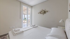 A bedroom with a bed, a nightstand, a lamp, a wall clock, and a sliding glass door leading to an outdoor area.