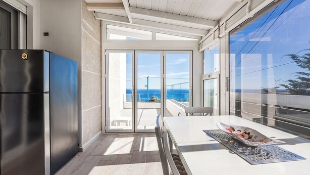 A modern kitchen with a stainless steel refrigerator, a glass door leading to a balcony with a view of the sea.