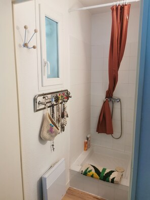 Eine Dusche mit brauner Duschvorhang, ein Handtuchhalter mit Taschen und Schmuck, und ein Fenster mit Blick auf Blau.
