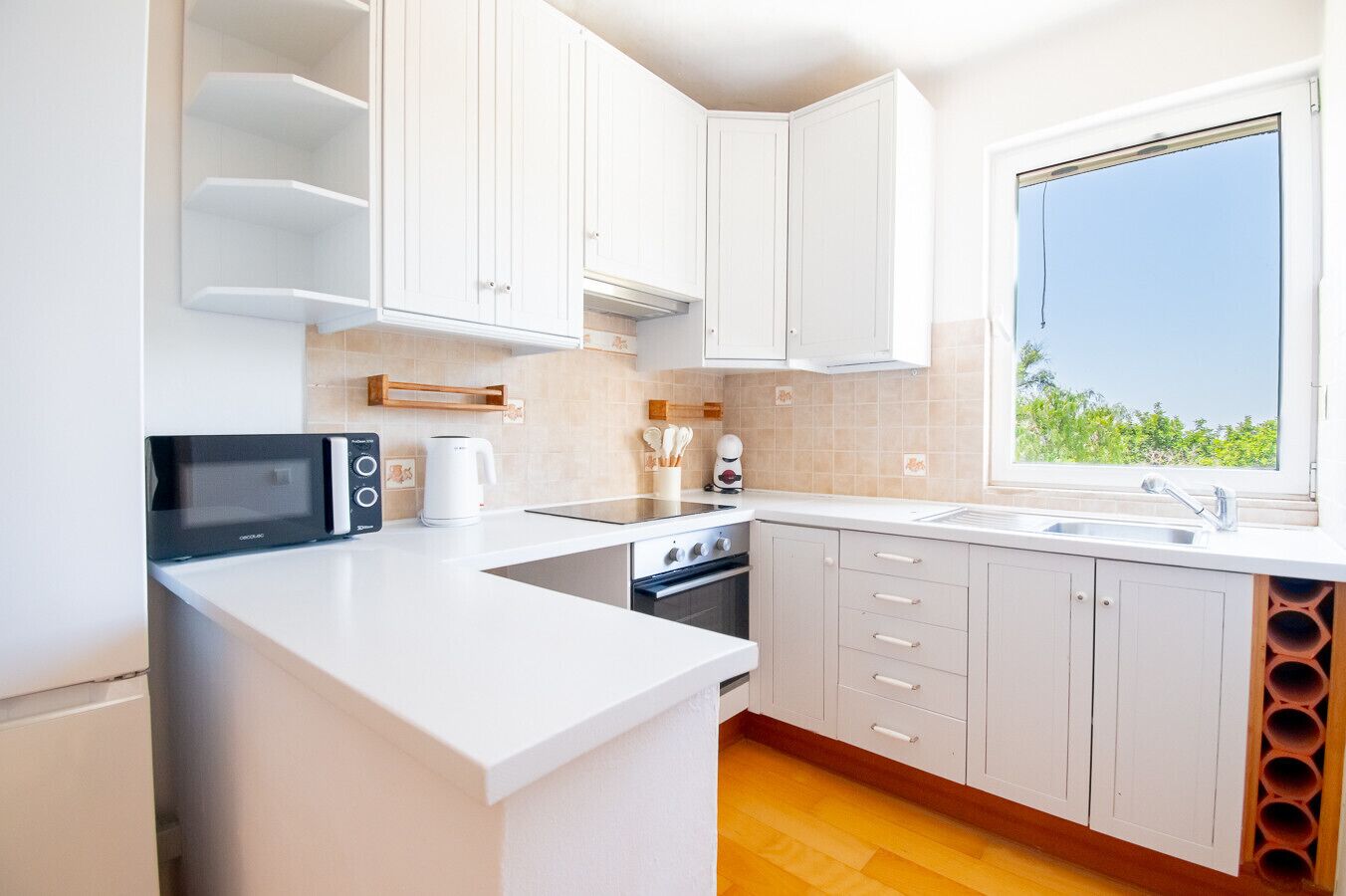 Una cocina moderna con armarios blancos, horno empotrado, microondas y un amplio ventanal con vistas.