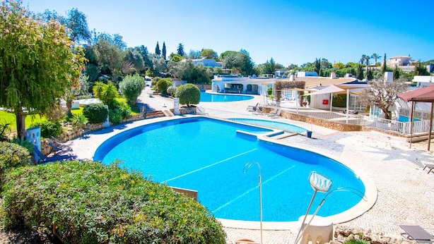 Ein großer Pool im Freien, umgeben von einem angelegten Garten, mit Blick auf Wohnhäuser im Hintergrund.