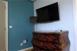Ein Zimmer mit türkisfarbenen Wänden, einem flachbildfernseher über einer Holzkommode mit aufwendigen Schnitzereien und einer Lampe neben der Kommode.