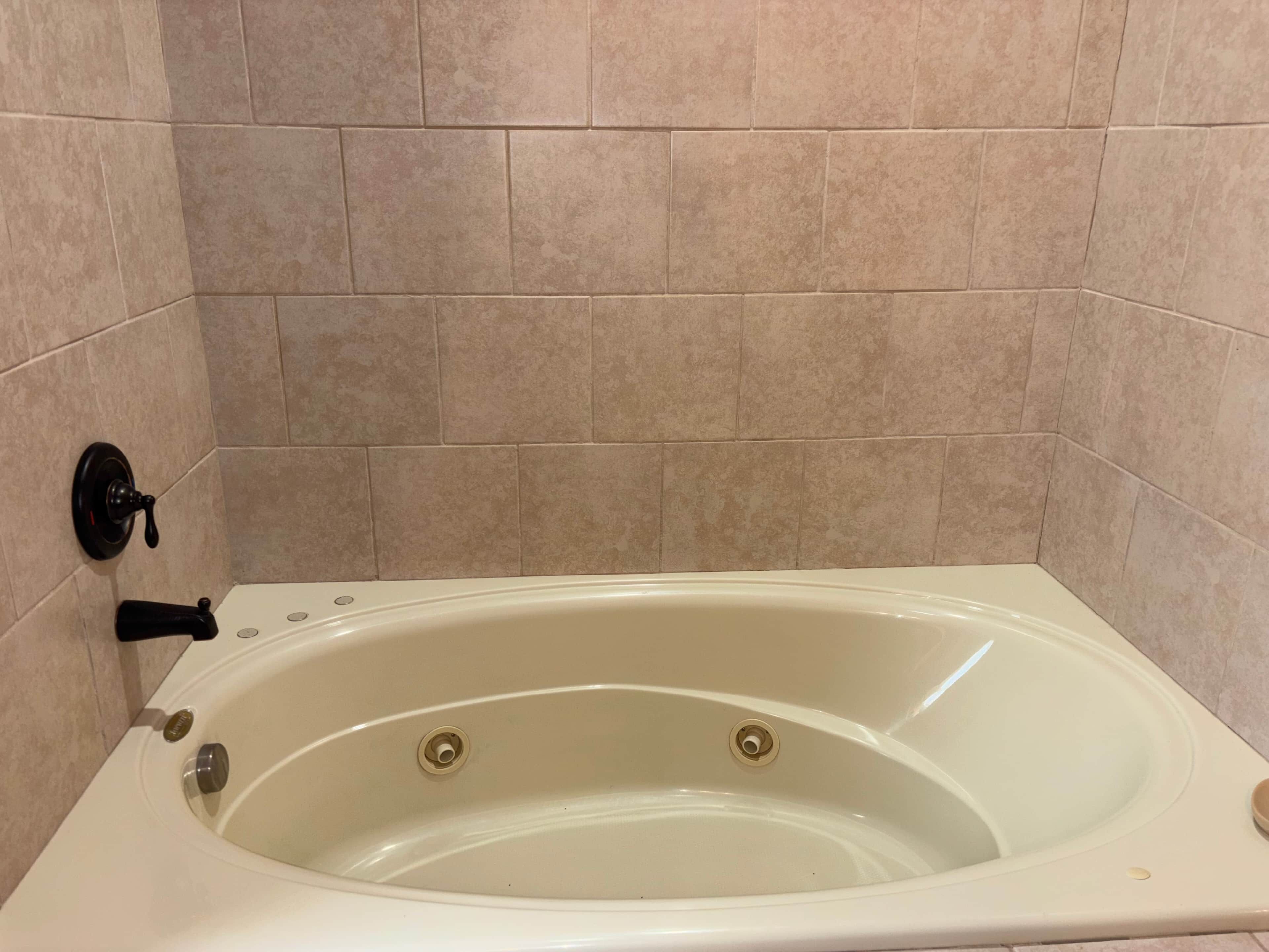 A bathtub with a control knob, a faucet, and a drain.