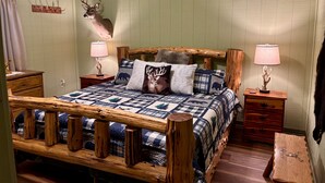 A rustic bedroom with a wooden bed frame, two bedside lamps, a deer head mounted on the wall, and a quilted bedspread.