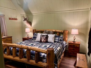 A rustic bedroom with a wooden bed frame, two bedside lamps, a deer head mounted on the wall, and a quilted bedspread. - Antler Ridge - surrounded by nature & wildlife! (Page County)