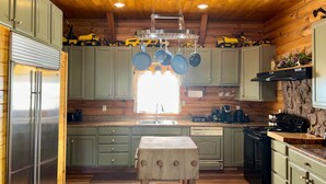 A kitchen with wooden cabinets, a stainless steel refrigerator, hanging pots, a coffee bar, and a stone accent wall.