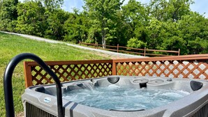 A hot tub with a wooden deck and a view of a grassy area with trees.