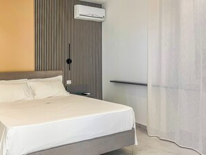 Una camera d'albergo con un letto, un comodino, un condizionatore d'aria a parete e una tenda.