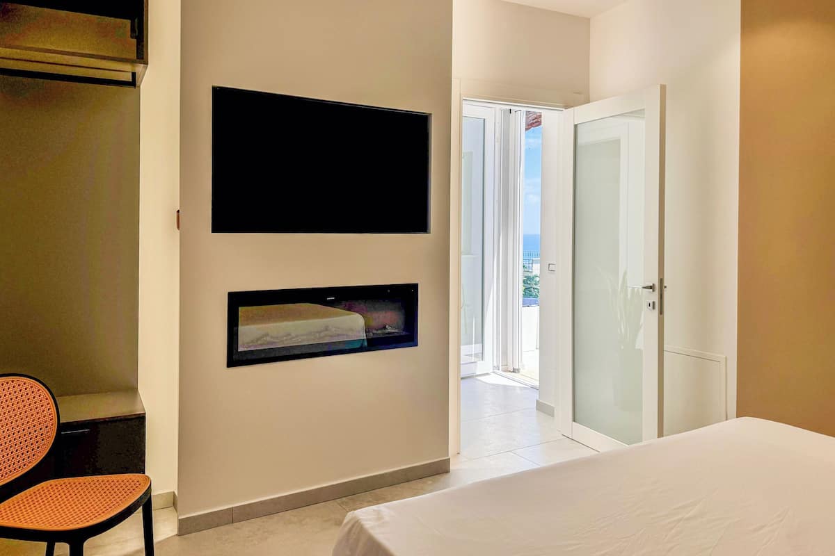 A bedroom with a bed, a TV mounted on the wall, a chair, and a door leading to a balcony.