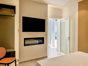 Una camera da letto con un letto, una TV a muro, una sedia e una porta che dà su un balcone.