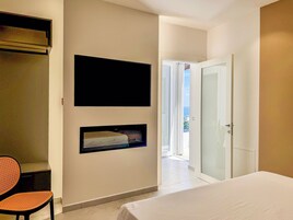 Una camera da letto con un letto, una TV a muro, una sedia e una porta che dà su un balcone.