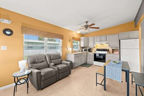 Ein kompakter Wohnbereich mit Sofa, Esstisch, Küchenzeile und Deckenventilator.