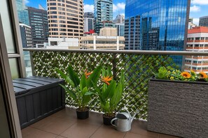 A balcony with potted plants, a metal watering can, and a view of a cityscape with modern buildings. - CBD Apt Sky Tower View by Zodiak Stays (Auckland Central)