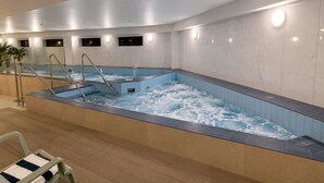 Ein großes Hallenbad mit Stufen zum hineinsteigen, umgeben von Wänden mit eingelassener Beleuchtung.