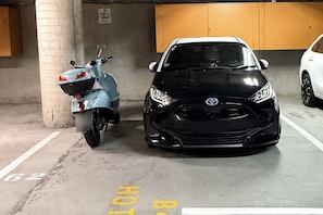 A parking garage with a scooter and a black car parked next to each other. - CBD Apt Sky Tower View by Zodiak Stays (Auckland Central)