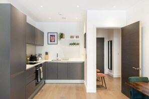 A modern kitchen with grey cabinets, a white countertop, and a small dining area with a wooden table and two chairs. - GuestReady - Chic Urban Retreat with Balcony | 20min Oxford Circus (London)