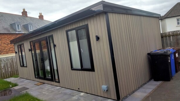 A modern, single-story building with large windows, a flat roof, and a paved patio area.