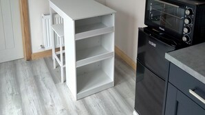 A kitchen with a white countertop, a black oven, and a white shelving unit.