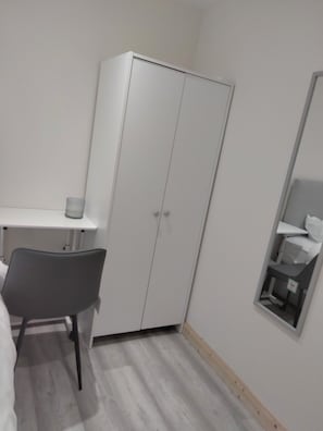 Ein Schlafzimmer mit Bett, Schreibtisch, Stuhl, Kleiderschrank und Spiegel.