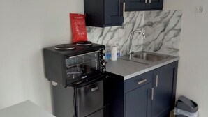 A compact kitchen with dark cabinets, a built-in microwave, a sink, and a trash bin.