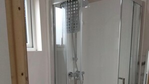 A bathroom with a glass-enclosed shower, a toilet, and a window.