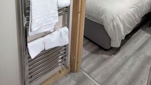 A hotel room with a bed, a towel rack, and a wooden floor.