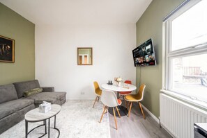 Ein Wohnzimmer mit einer Couch, einem runden Tisch mit Stühlen, einem an der Wand montierten Fernseher und einem Fenster mit Blick.