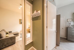 Ein Zimmer mit einer Couch, einem Spiegel, einem Regal mit Haken, einer Tür und einem Schrank.