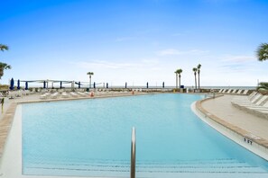 Ein großer Pool mit Liegestühlen und Palmen, umgeben von einer Sonnenterrasse.