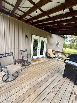 A covered deck with a grill, two rocking chairs, and a door leading to a covered area. - Secluded Ranch Stay w/ Views | 2BR/2BA (Walnut Shade)