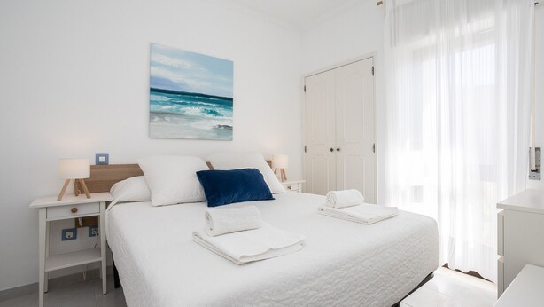 Um quarto bem arrumado com cama, mesas de cabeceira, um criado-mudo, um quadro e um guarda-roupa.