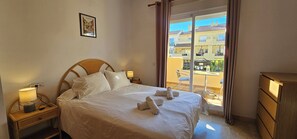 A hotel room with a bed, bedside lamps, a window with a view of buildings, and a wooden dresser.