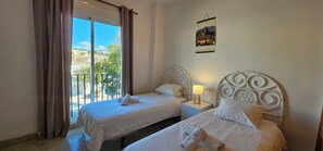 Une chambre d’hôtel avec deux lits, un balcon, un tableau et une table de chevet avec une lampe.