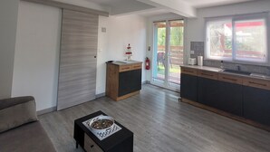 A modern living room with a sofa, a coffee table, and a kitchen area with a sink and cabinets. - Pom Kanel Vacation Rental with Unobstructed Views (Sainte-Anne)