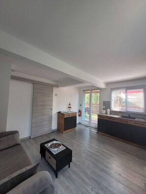 Ein modernes Wohnzimmer mit einer Couch, einem Couchtisch und einer Küchenzeile inklusive Spüle und Schr änken.