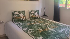 A bedroom with a bed, a painting of palm trees, a nightstand, a lamp, and a window with curtains. - Pom Kanel Vacation Rental with Unobstructed Views (Sainte-Anne)