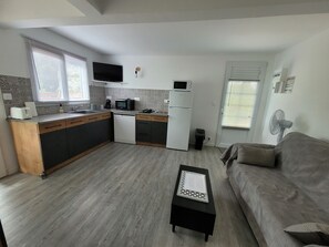 Eine kompakte Küche mit Mikrowelle, Toaster und Kühlschrank. Im Wohnbereich befindet sich ein kleiner Esstisch und ein Sofa.
