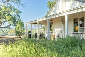Eine überdachte Veranda mit Stühlen und einer Laterne, umgeben von Grünpflanzen und Blick auf die Berge.