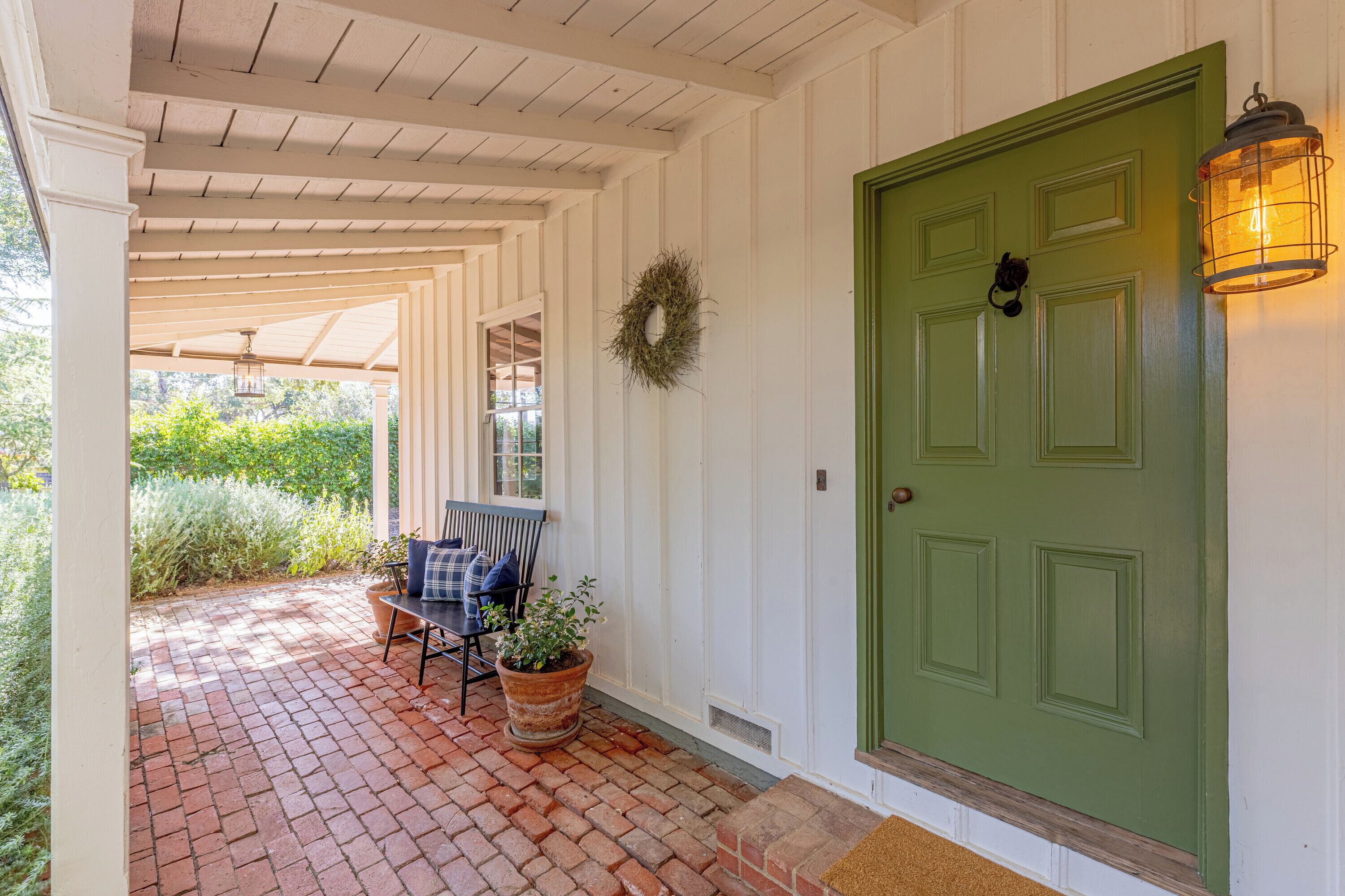 A covered porch with a green door, a potted plant, and a bench.